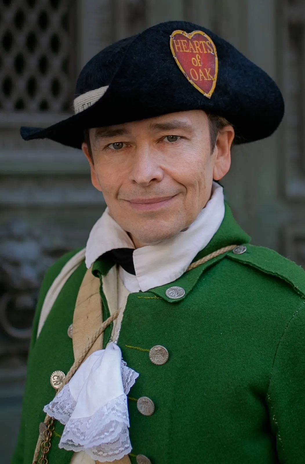 Scott in a green colonial coat with the Hearts of Oak emblem on his tricorn hat