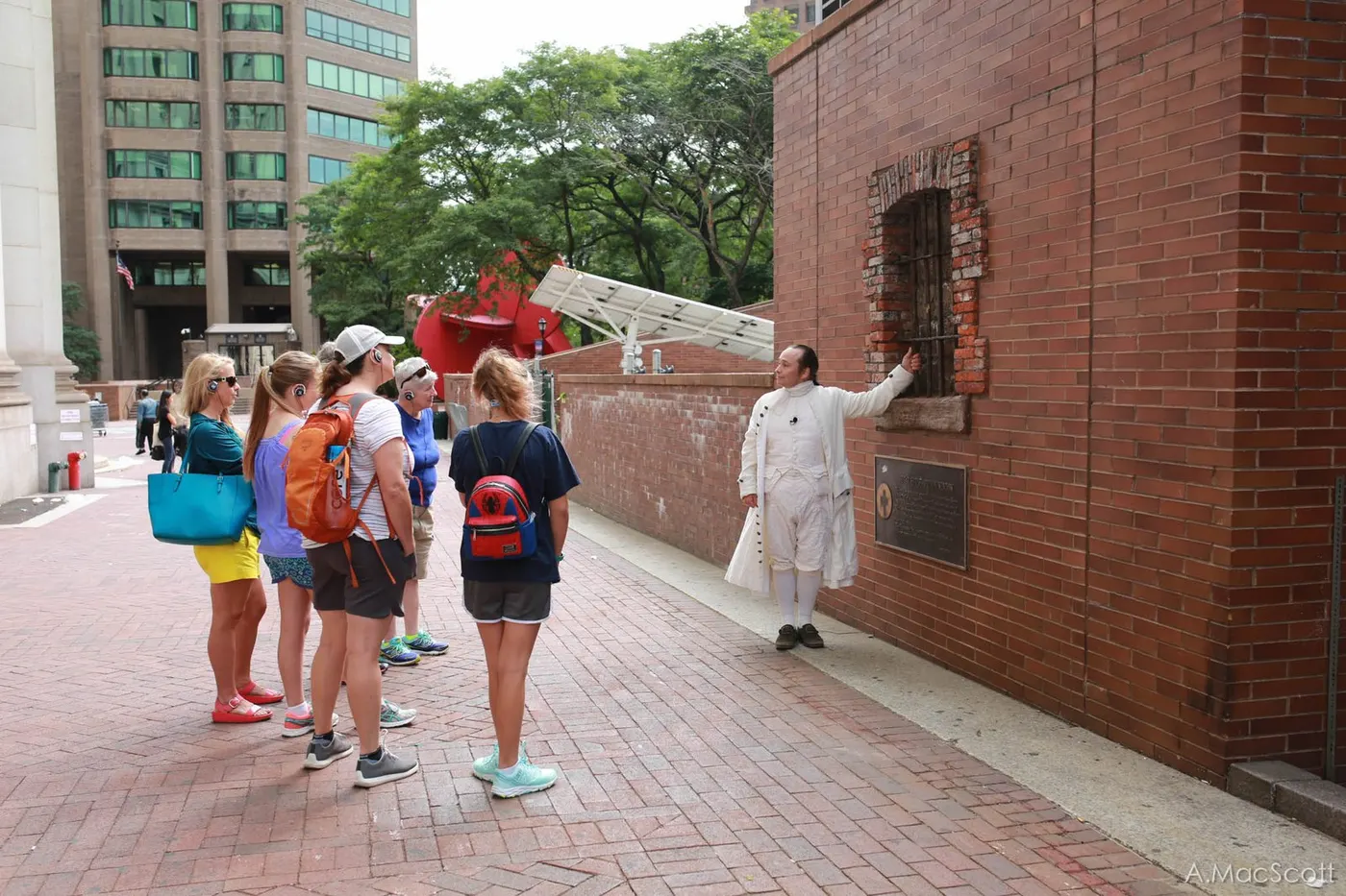 Hamilton addressing tour guests by a memorial wall