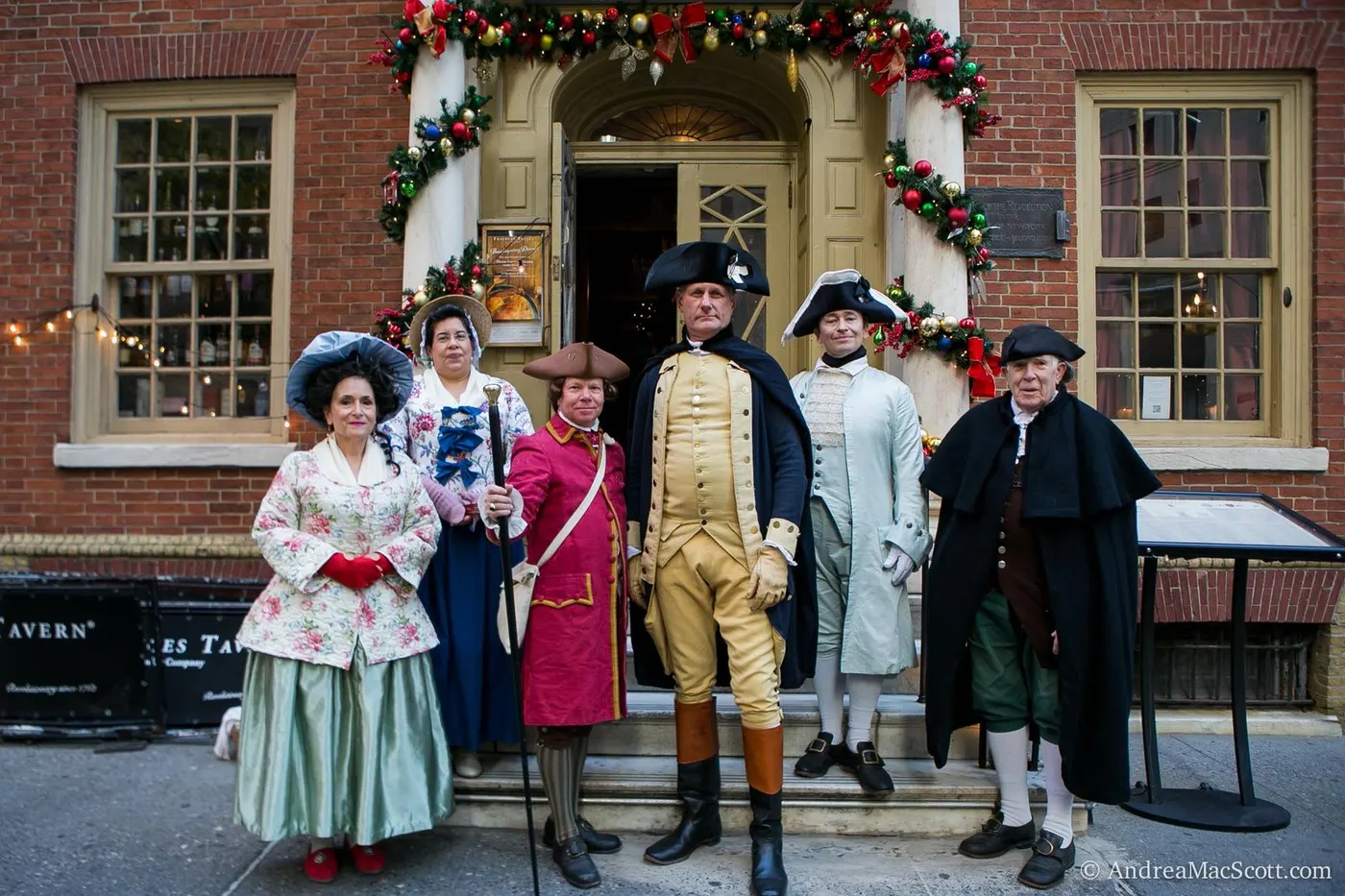 Colonial reenactors gathered before a decorated doorway